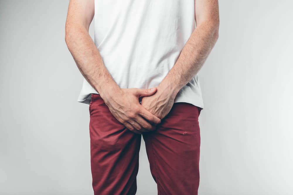 Caucasian man in white T-shirt and burgundy pants. Holds his hands on groin. Cut view. Concept. Isolated over light background.